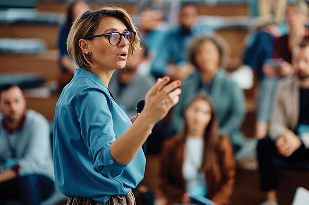 Mid adult businesswoman talking to group of seminar attendees in conference hall.